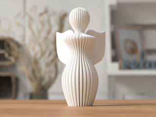 A white, abstract sculpture of an angel stands on a wooden surface protecting a smaller figure.