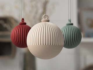 Three spherical ornaments in red, beige, and green hanging against a blurred background.