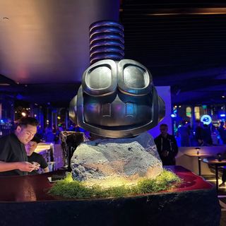 Decorative sculpture of a robot head on a rock with people in the background